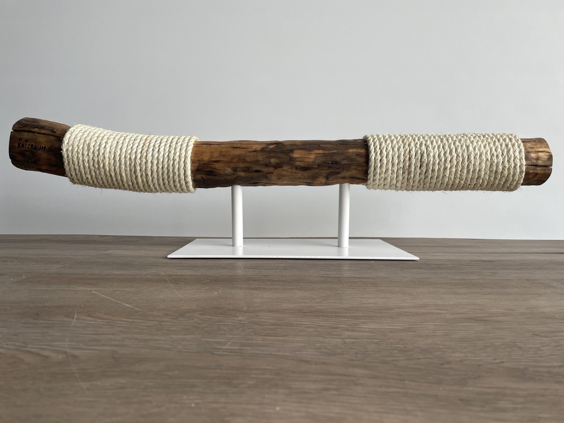 Horizontal liegender Naturholz-Kratzstamm auf einem eleganten weißen Metallgestell – modernes Katzendesign-Möbelstück der Katzbaum Manufaktur