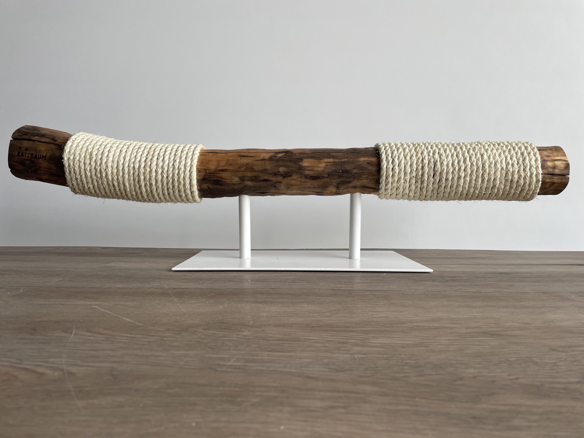 Handgefertigter horizontaler Kratzstamm aus massivem Naturholz auf einem modernen weißen Metallfuß – exklusives Katzendesign für minimalistische Wohnräume